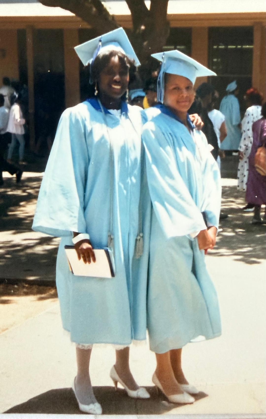 Two graduates in light blue caps and gowns holding diplomas on graduation day
