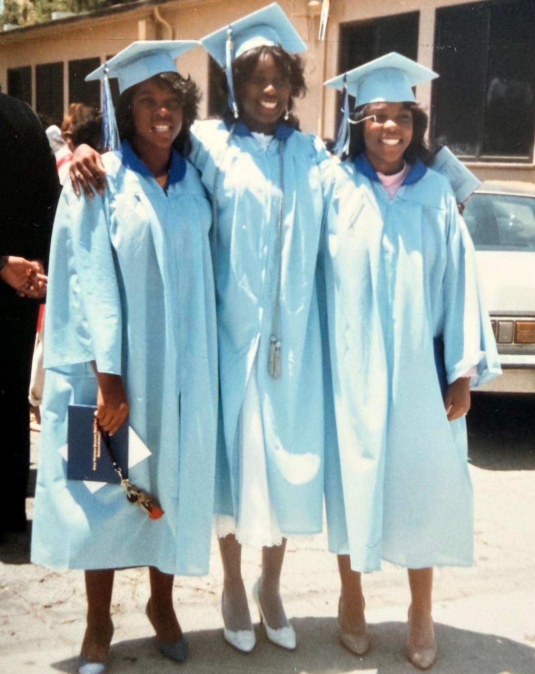 Three graduates in light blue caps and gowns celebrating on graduation day