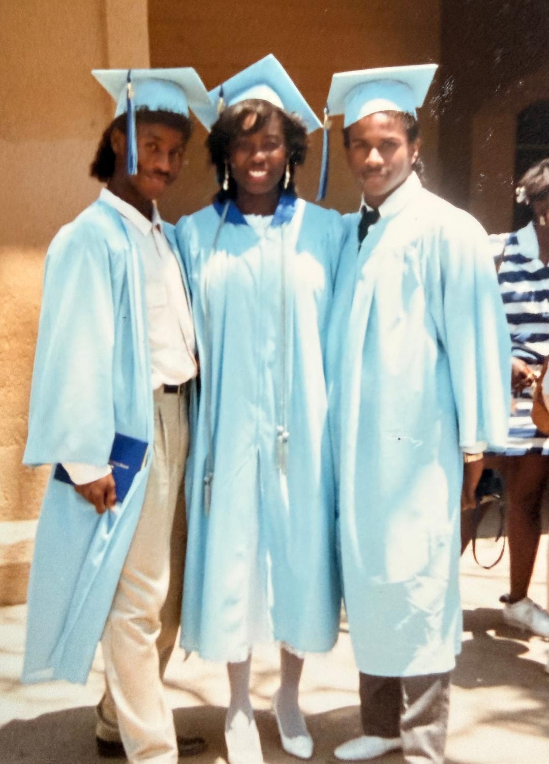 Three graduates in light blue caps and gowns posing together on graduation day