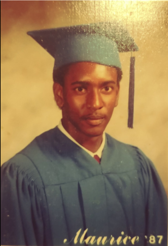 Maurice graduation portrait in blue cap and gown, Class of 1987