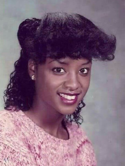 Young woman with curly hair in pink sweater yearbook portrait